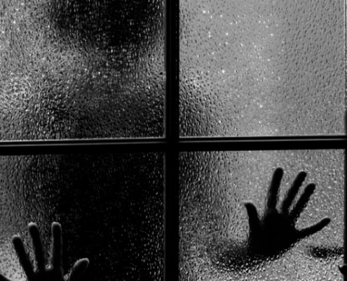 Silhouette scura di una persona con le mani appoggiate al vetro appannato di una finestra a quattro riquadri