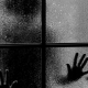 Silhouette scura di una persona con le mani appoggiate al vetro appannato di una finestra a quattro riquadri