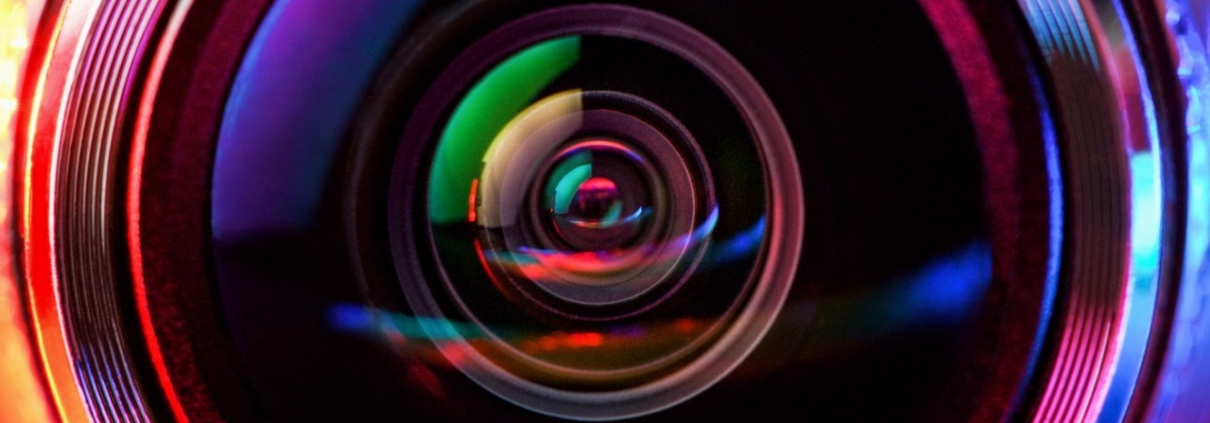 Primo piano macro di un obiettivo fotografico con riflessi rossi e blu, simbolo di bonifica e controllo ambientale