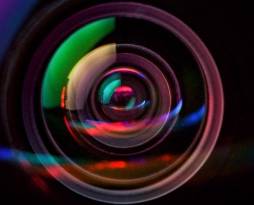 Primo piano macro di un obiettivo fotografico con riflessi rossi e blu, simbolo di bonifica e controllo ambientale