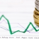 Pila di monete su grafici finanziari e tabelle di analisi economica per indagini patrimoniali