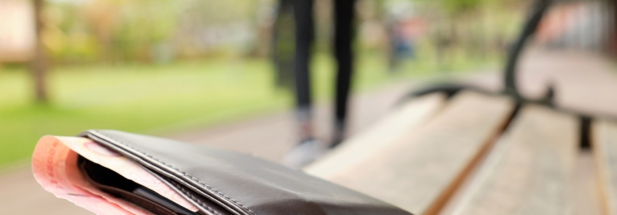 Portafoglio nero con banconote lasciato su una panchina di parco, con una persona che si allontana sfocata